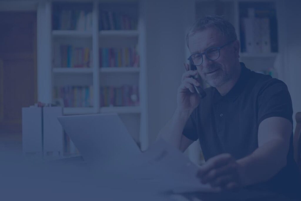 Professional man working from home, engaged in a business call while reviewing documents on his laptop, reflecting productivity and remote work efficiency.