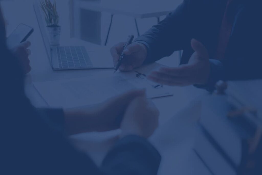 Business meeting with professionals discussing and signing documents at a desk, with a laptop and office supplies in the background.